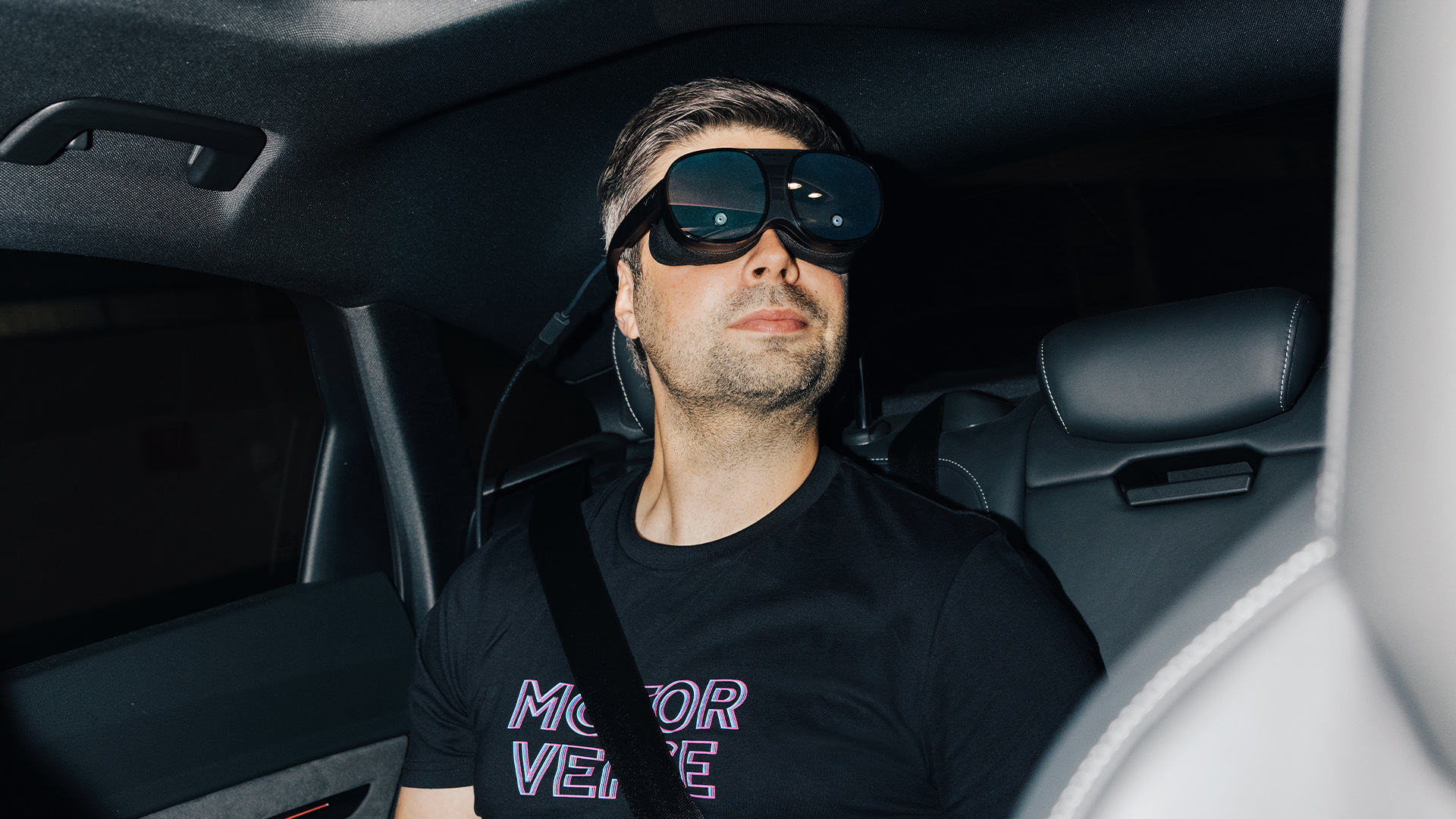 Nils Wollny sitting in the back seat of an Audi wearing VR goggles.